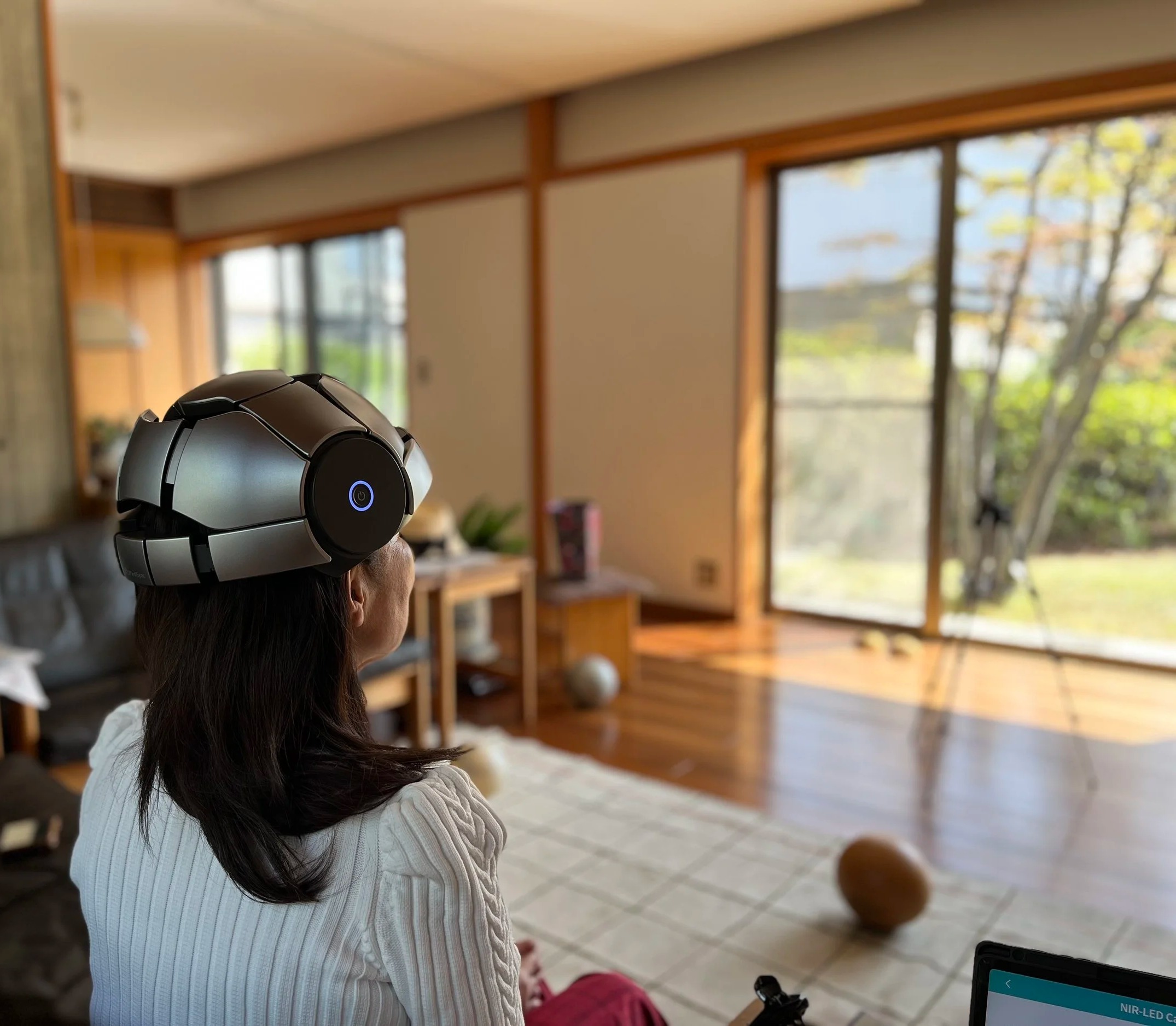 A woman wearing the iSyncWave headset during a near-infrared PBM light therapy session at home